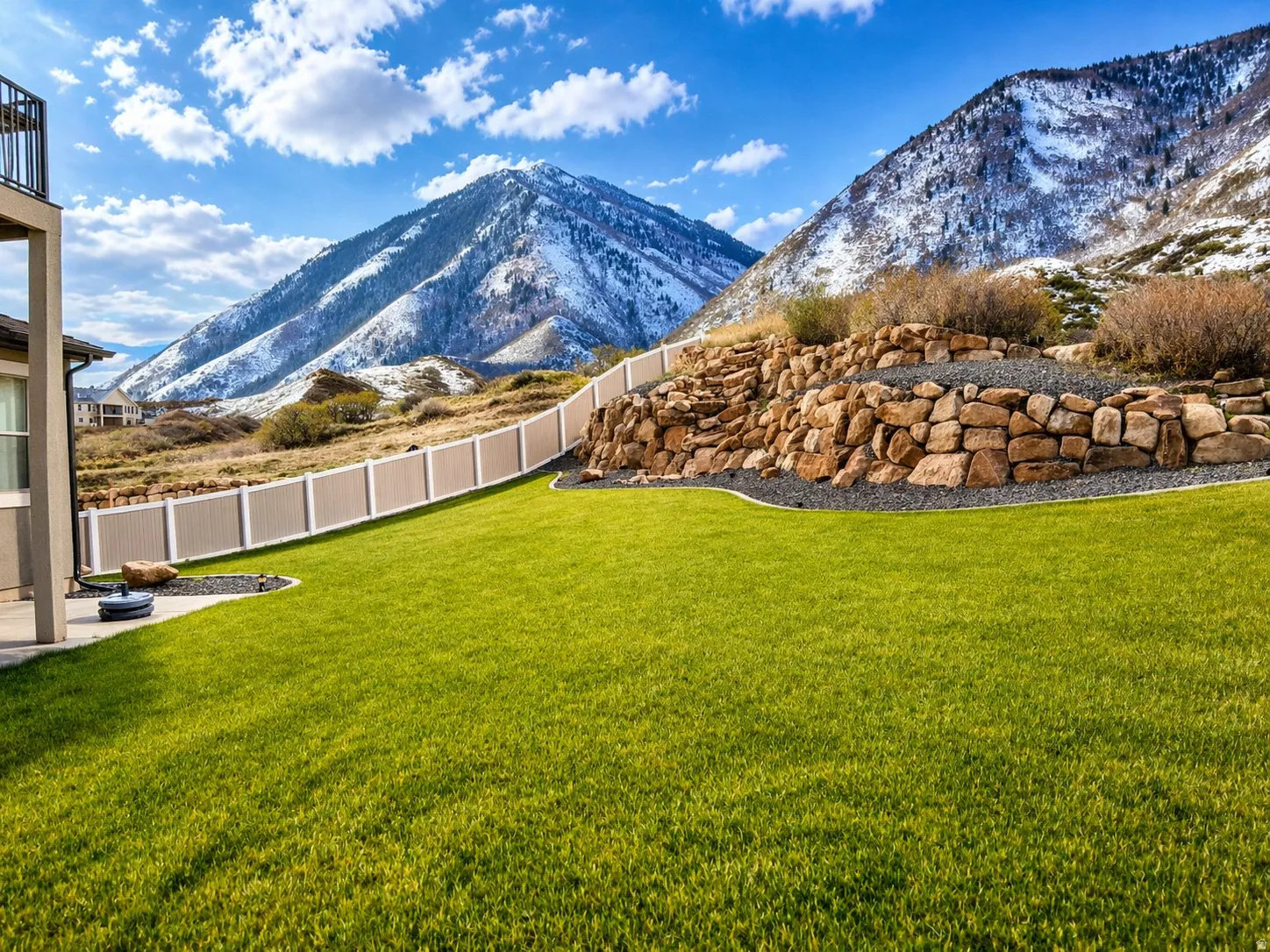 Expansive green lawn featuring a decorative rock retaining wall, a multi-tone privacy fence, and a concrete patio space