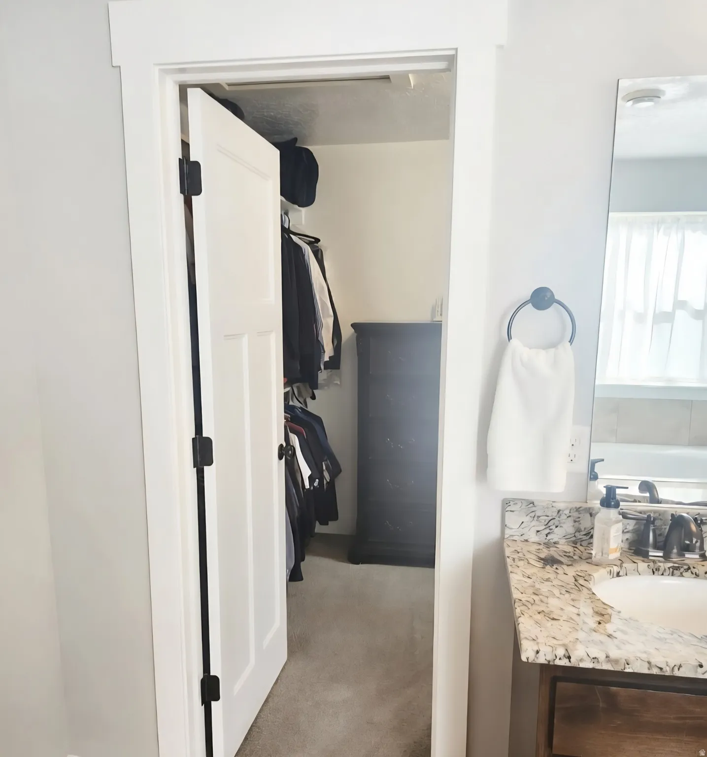 Walk-in closet with carpet flooring and built-in shelving, accessible from a bathroom featuring a granite-style countertop vanity with an undermount sink and dark bronze faucet