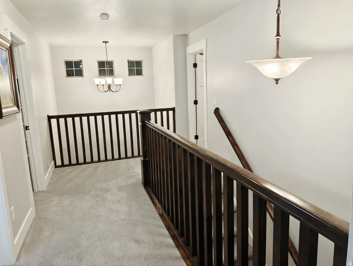 Upper-level landing featuring plush gray carpeting, dark wood balusters and handrails, and a contemporary chandelier