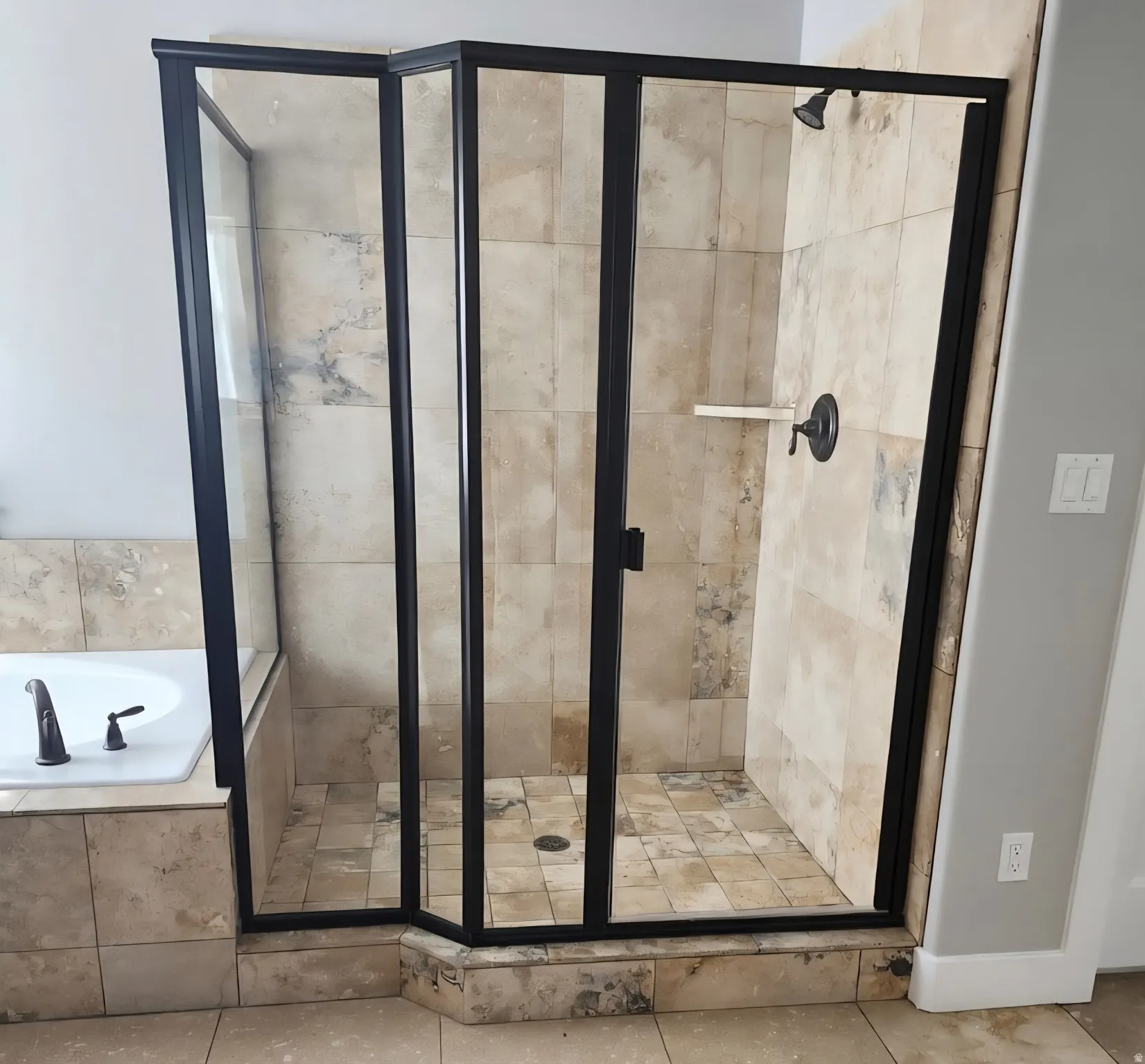Glass-enclosed shower with black framing, tiled walls, and a built-in shelf