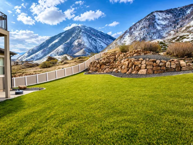 Expansive green lawn featuring a decorative rock retaining wall, a multi-tone privacy fence, and a concrete patio space