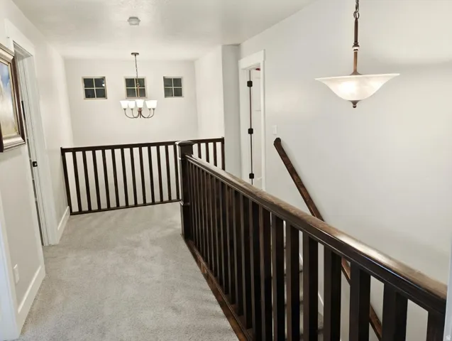 Upper-level landing featuring plush gray carpeting, dark wood balusters and handrails, and a contemporary chandelier