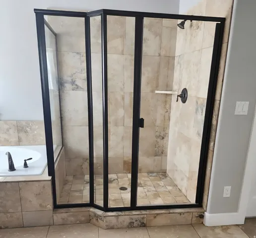 Glass-enclosed shower with black framing, tiled walls, and a built-in shelf