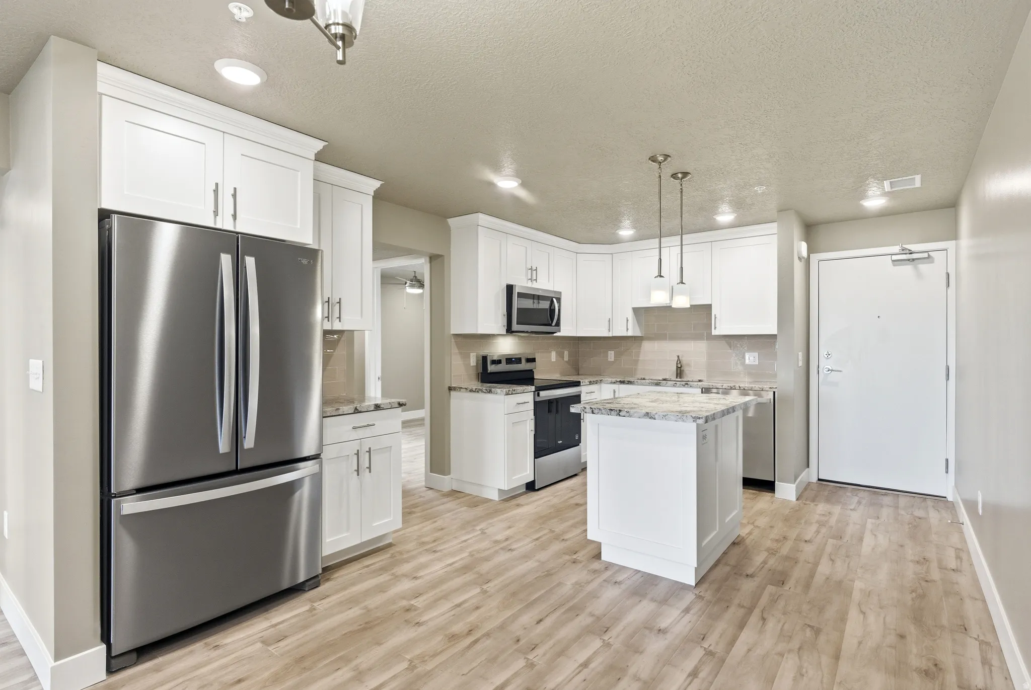 Kitchen with stainless steel appliances, a kitchen island, decorative light fixtures, white cabinets, and tasteful backsplash