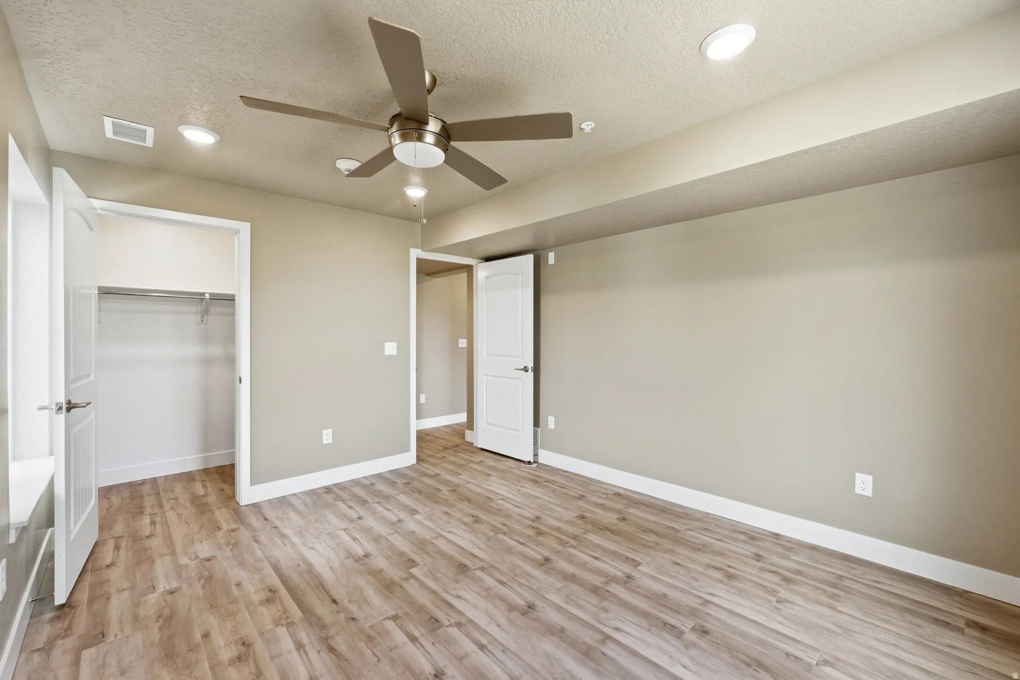 Bedroom featuring light wood-style floors, a textured ceiling, ceiling fan, recessed lighting, and a spacious closet