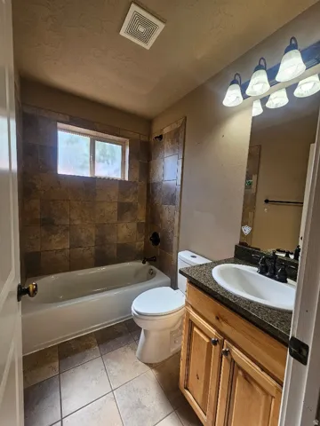 Bathroom featuring a tiled shower surround, built-in bathtub, natural wood vanity with a stone countertop, and ceramic tile flooring