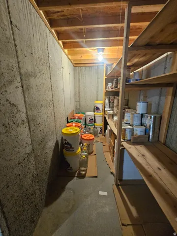 Cold Storage Unfinished basement area featuring concrete walls and flooring, exposed ceiling joists, and integrated wooden shelving