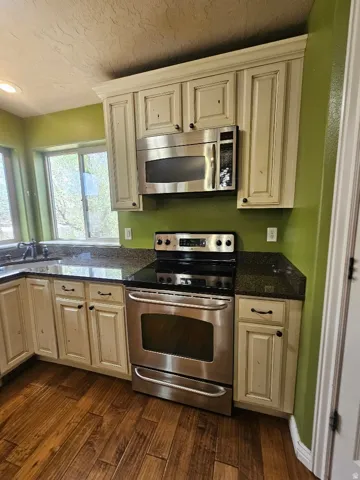 Kitchen featuring stainless steel appliances, dark stone countertops, cream-finished cabinetry, and wood-finish flooring