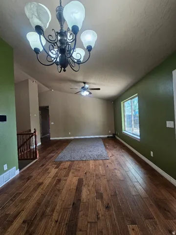 Spacious room featuring wood-finish flooring, a decorative chandelier, vaulted ceilings, and a ceiling fan