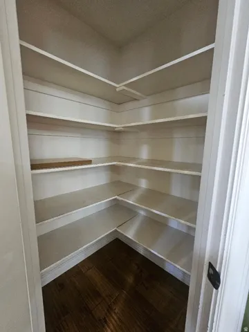 Corner pantry featuring multiple white built-in shelves and dark wood-finish flooring