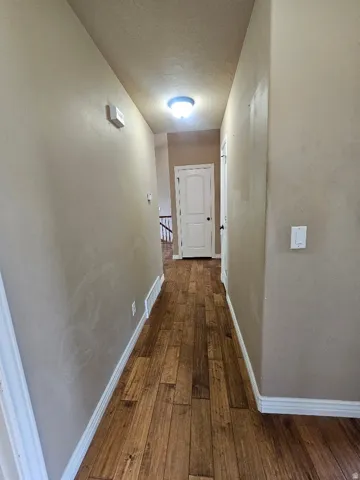 Hallway featuring wood-finish flooring, light tan wall color, white baseboards, and a flush-mount ceiling light fixture