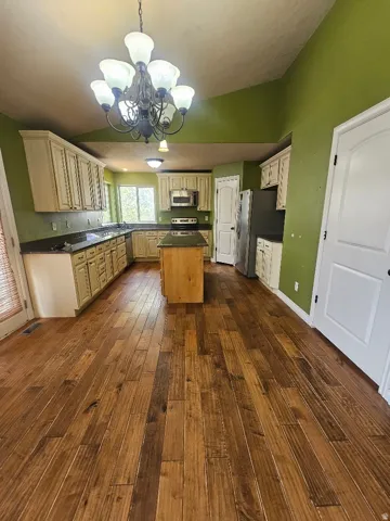 Spacious kitchen featuring extensive wood-finish flooring, a central island with countertop, perimeter cabinetry, dark countertops, and stainless steel appliances