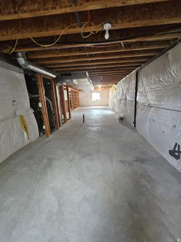 Unfinished basement featuring a concrete floor, exposed ceiling joists, and a visible window opening