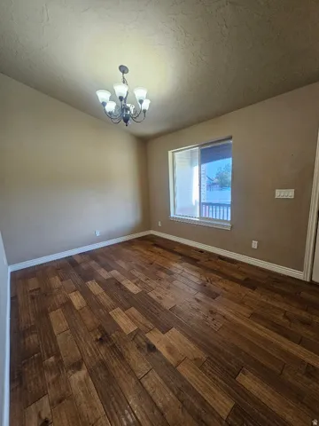Expansive room featuring wood-finish flooring, a contemporary five-light chandelier, and a large window with blinds