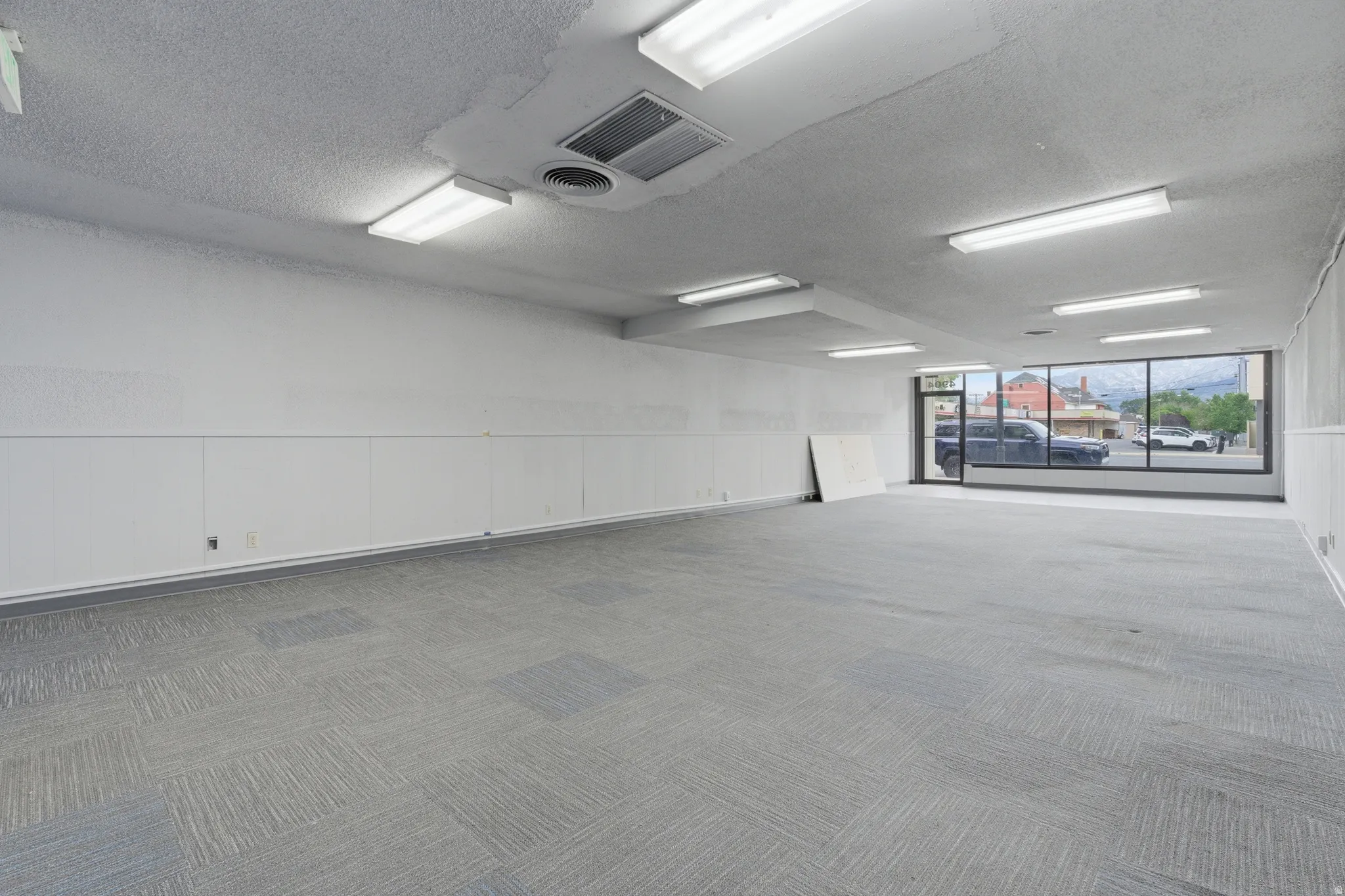 Spacious commercial interior featuring patterned carpet flooring and ample overhead fluorescent lighting