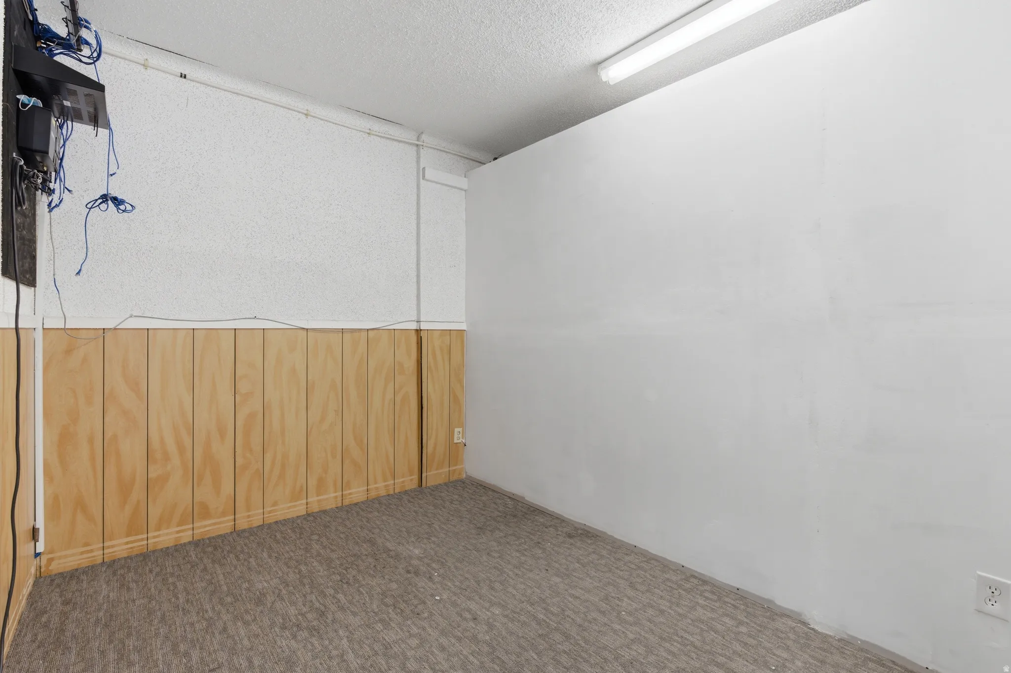 Room with textured white walls, wood paneling, and a drop ceiling with fluorescent lighting