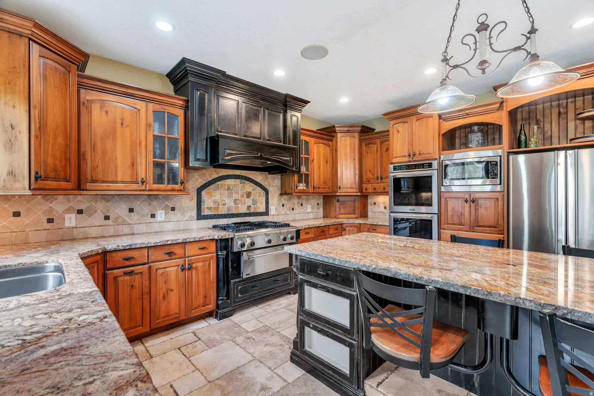 Two tone kitchen with light stone countertops, decorative light fixtures, a kitchen bar, stainless steel appliances, and glass fronted cabinets