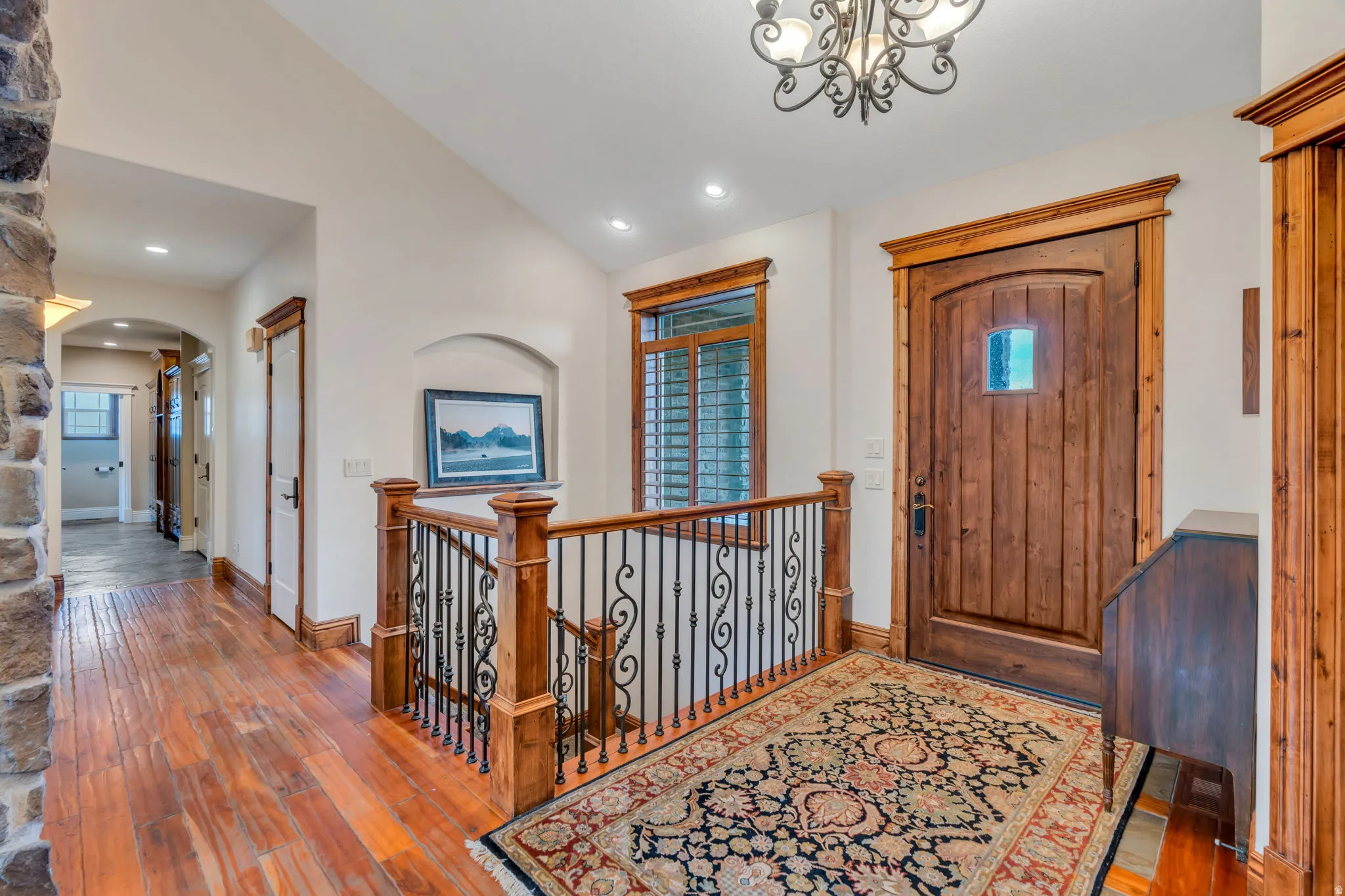 Foyer entrance with hardwood / wood-style floors, lofted ceiling, arched walkways, and a chandelier