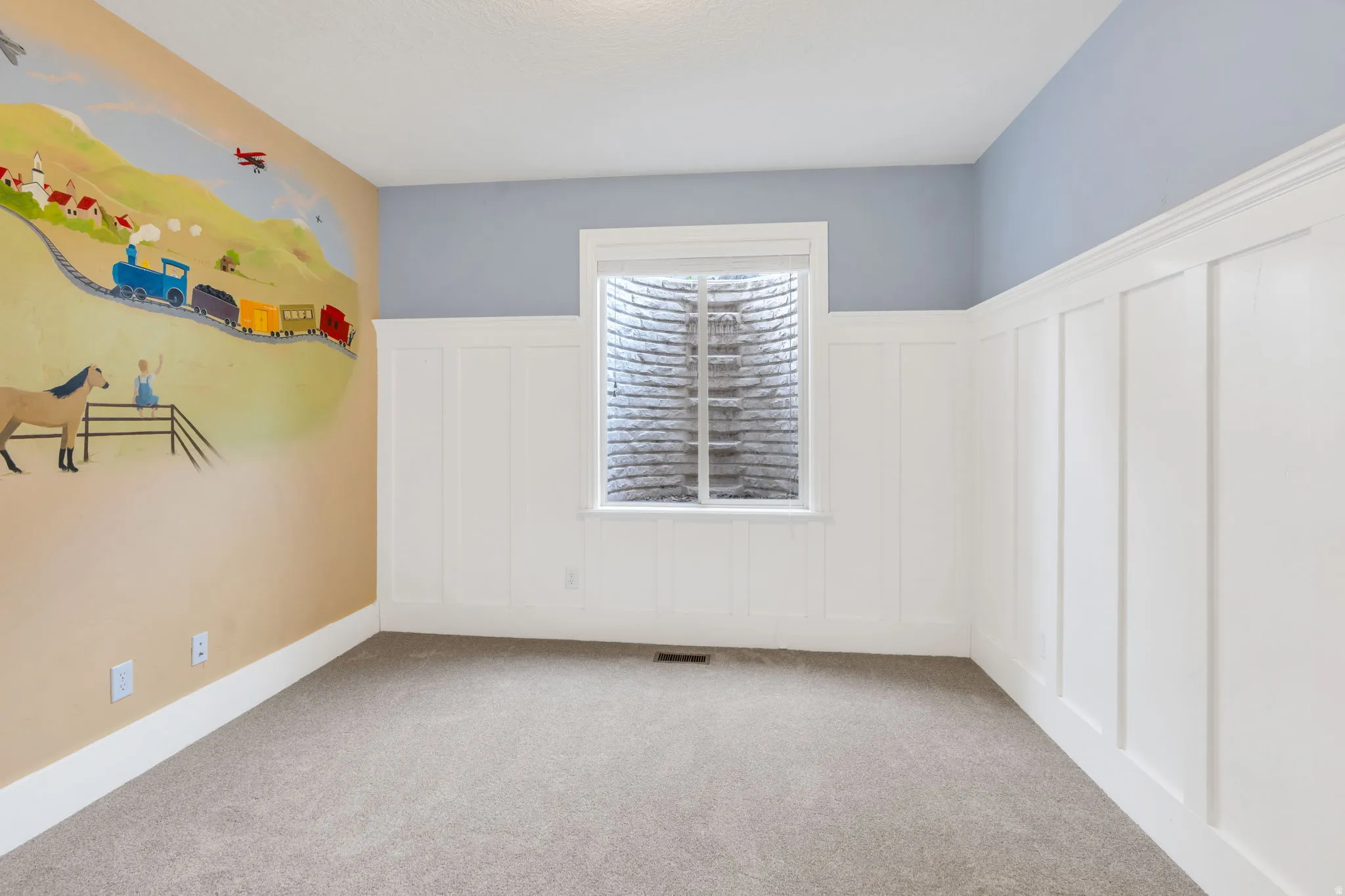 Empty room featuring a decorative wall, a wainscoted wall, and light carpet