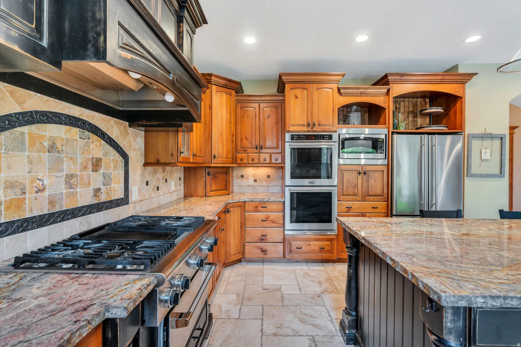 Dual tone kitchen featuring light stone counters, stainless steel appliances, range hood, stone tile floors, and recessed lighting