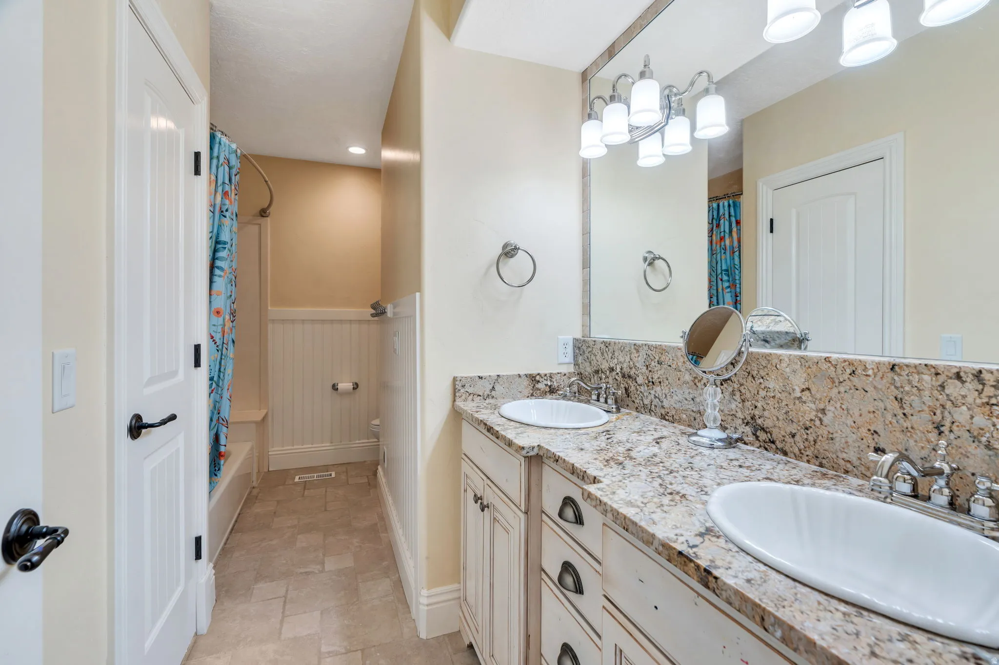 Full bathroom featuring double vanity, a wainscoted wall, light stone finish floors, recessed lighting, and shower / bathtub combination with curtain