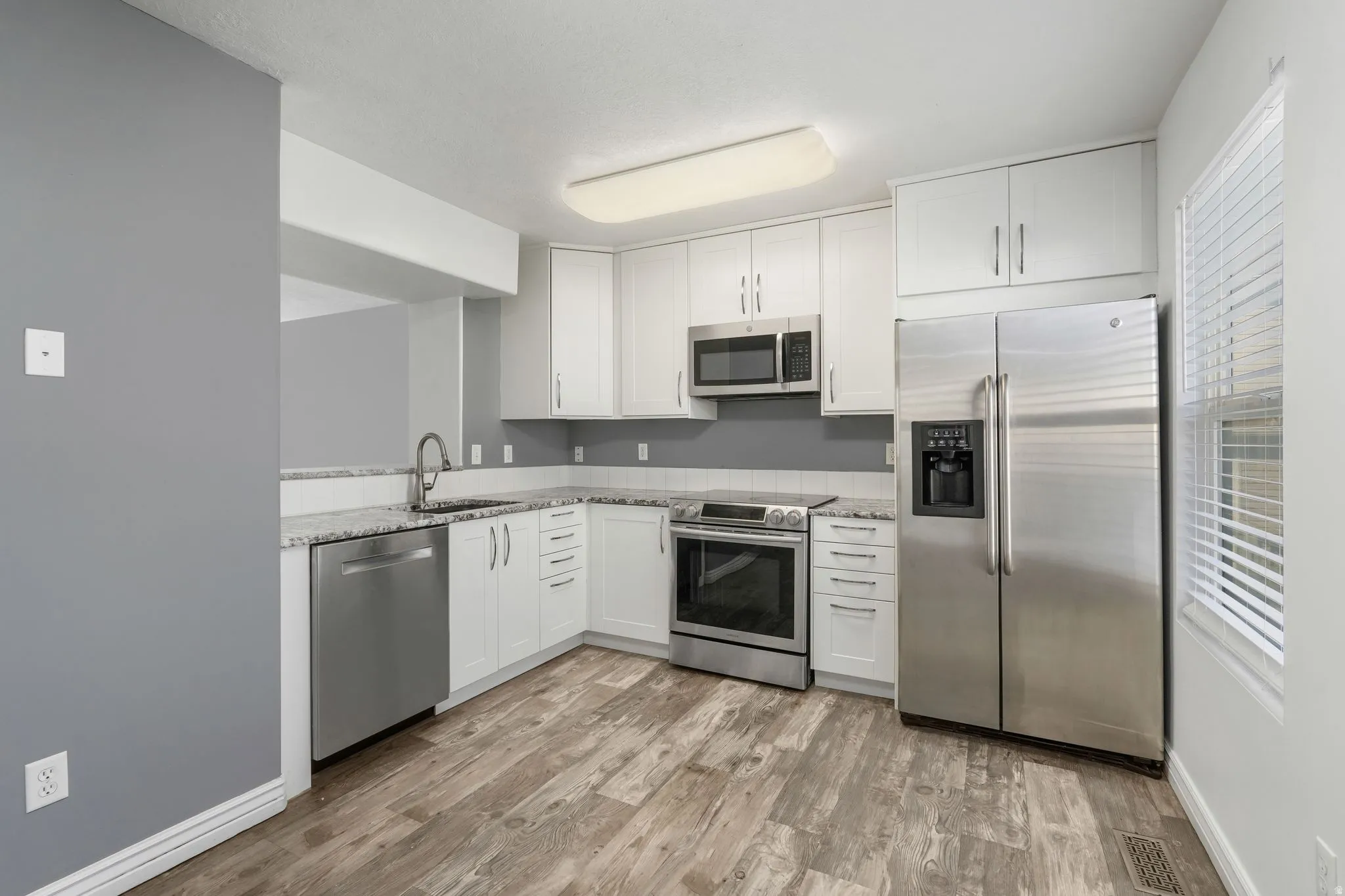 Kitchen with stainless steel appliances, white cabinets, light stone counters, and light wood finished floors