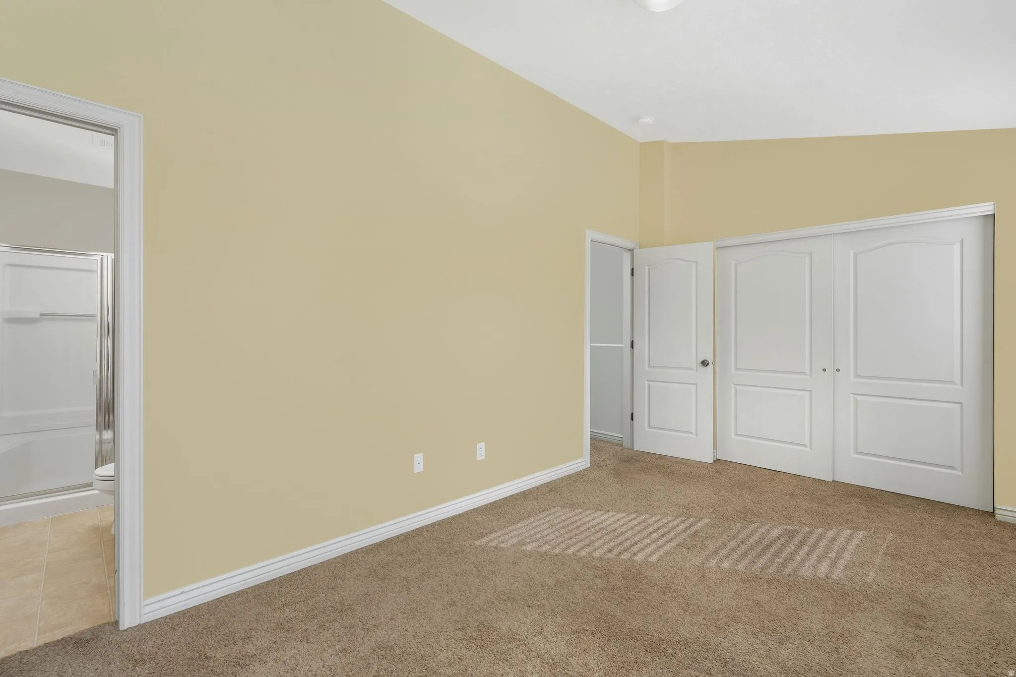 Primary bedroom with light carpet, lofted ceiling, a closet, and connected bathroom