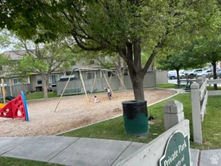 Private park featuring a playground with swings and a slide structure, wood chip surfacing, perimeter fencing, and mature trees providing shade