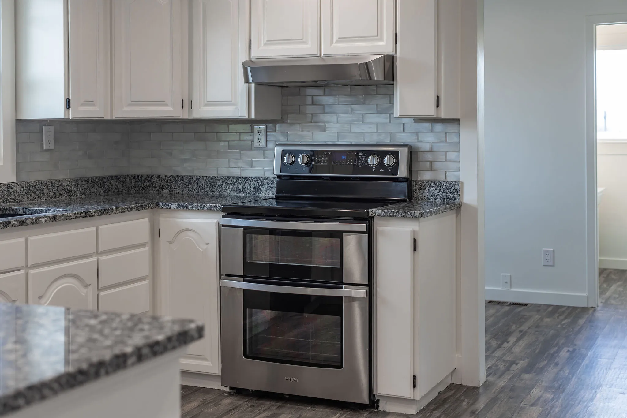 Kitchen featuring dark stone counters, double oven range, white cabinetry, and dark wood-style flooring