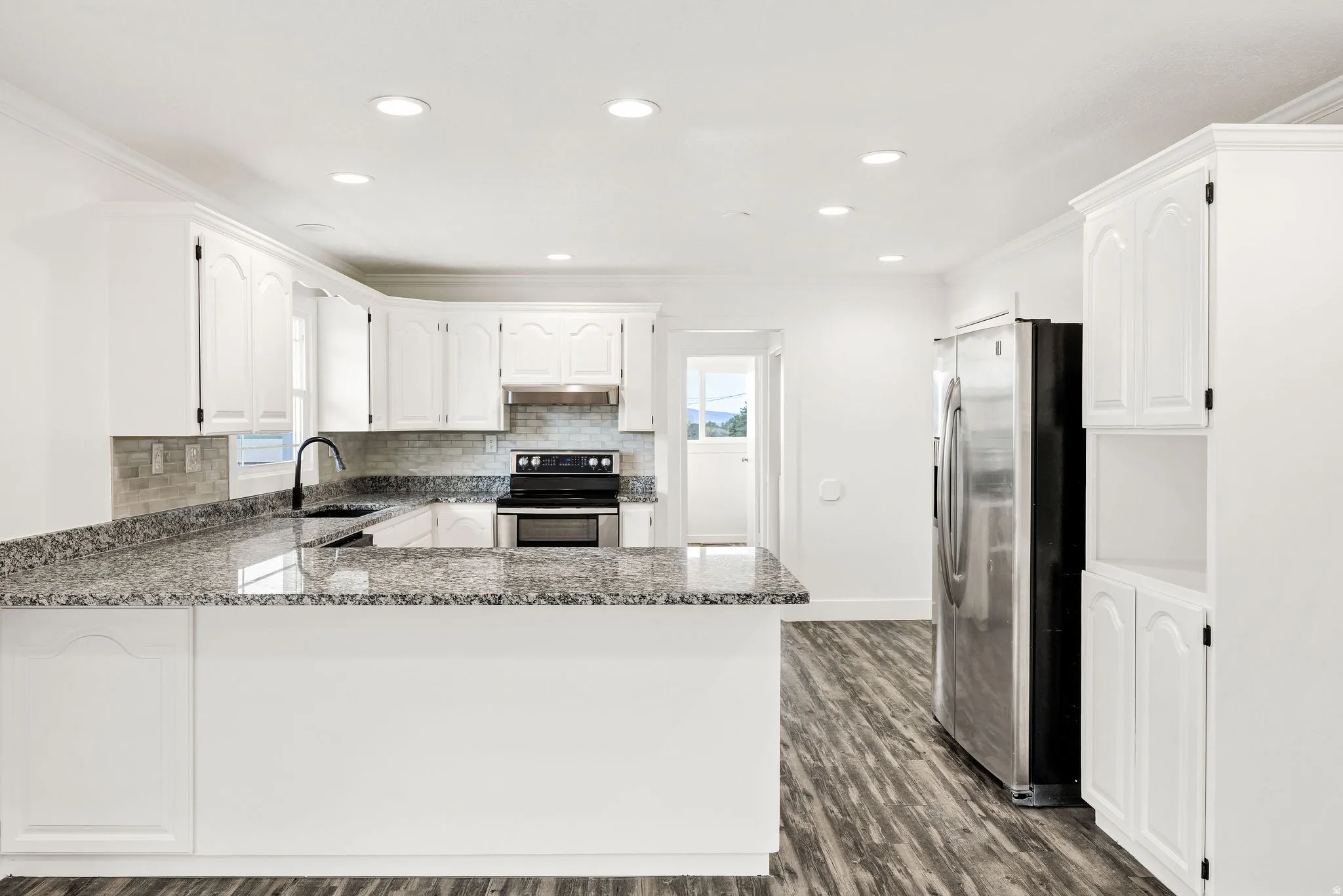 Kitchen with a peninsula, stainless steel appliances, white cabinets, dark wood-style flooring, and dark stone counters