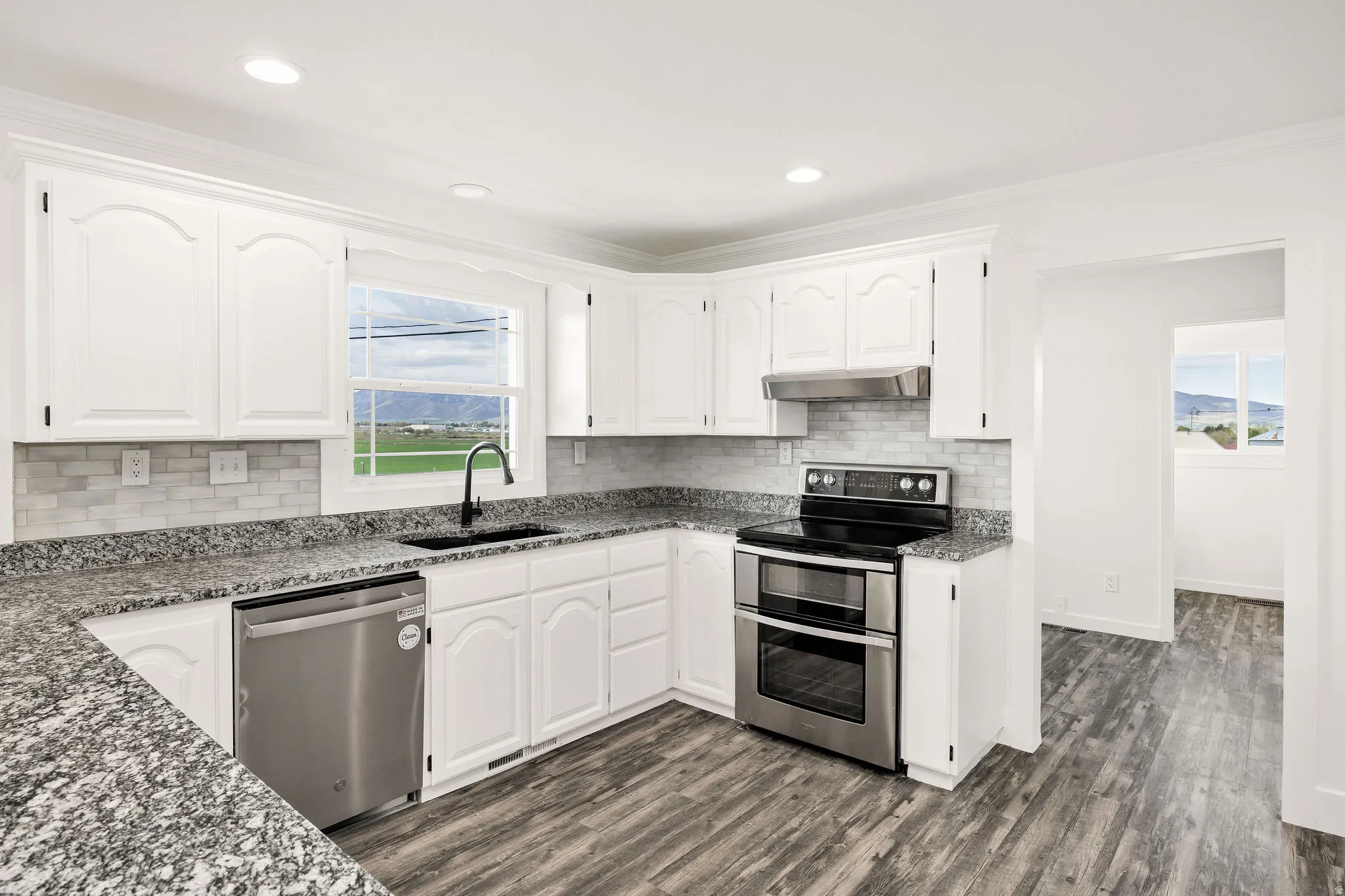 Kitchen with stainless steel appliances, dark stone counters, white cabinets, ornamental molding, and recessed lighting