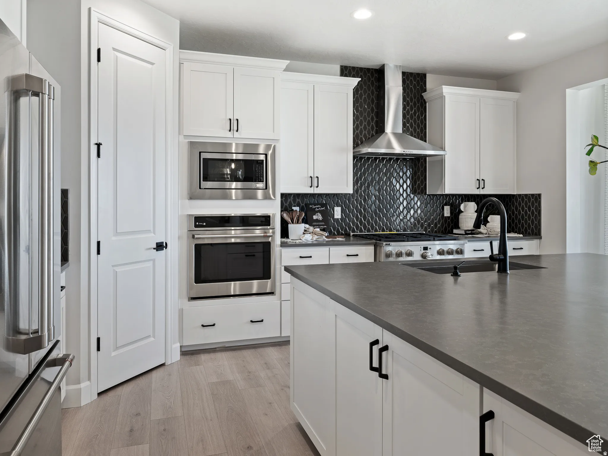 Kitchen featuring white cabinetry, stainless steel appliances, light wood-style flooring, backsplash, and recessed lighting