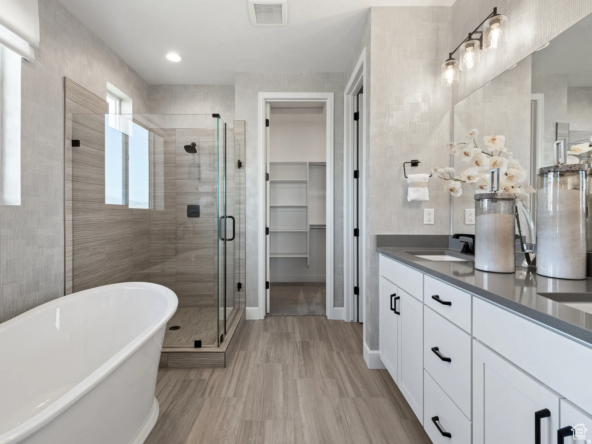 Full bathroom featuring double vanity, a shower stall, a soaking tub, a spacious closet, and light wood finished floors