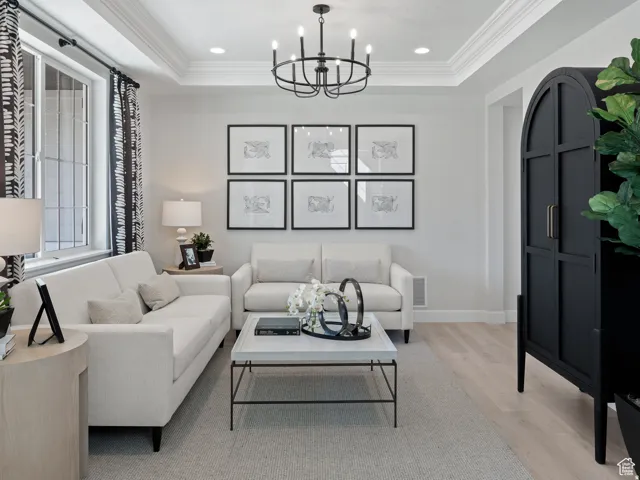 Living area featuring light wood-style floors, a raised ceiling, a chandelier, and ornamental molding