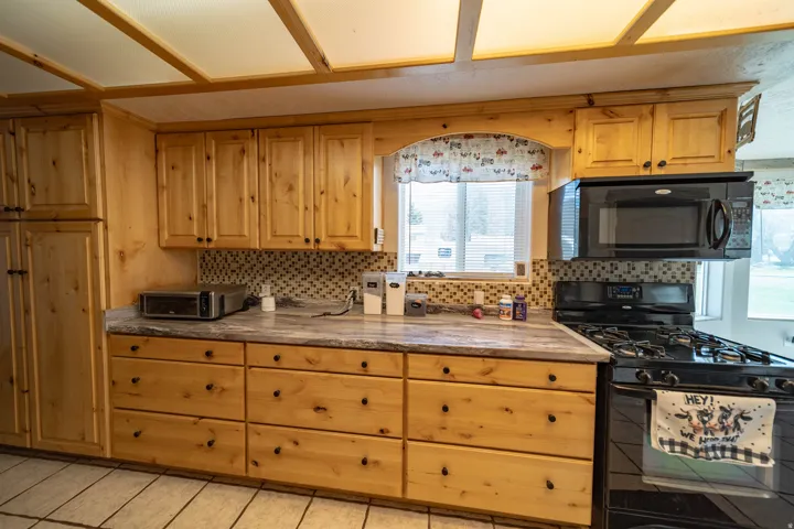 Kitchen featuring black appliances, backsplash, light countertops, and light wood finish cabinets