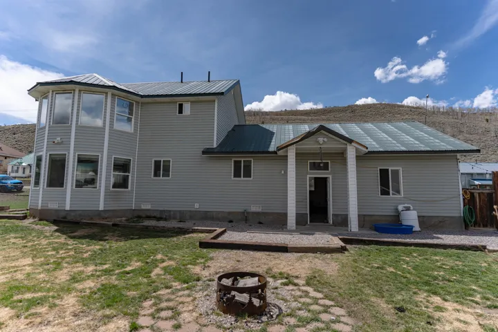 Rear view of house with a metal roof, a patio area, a lawn, and an outdoor fire pit