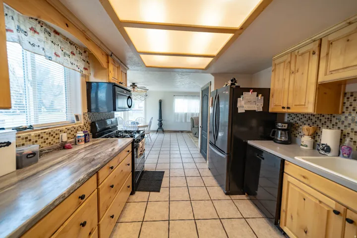 Kitchen with backsplash, black appliances, light wood finish cabinetry, and light countertops