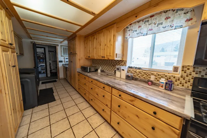 Kitchen with light tile patterned floors, black gas range oven, decorative backsplash, and light stone counters