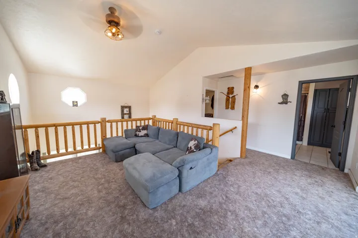 Carpeted living room with lofted ceiling and ceiling fan