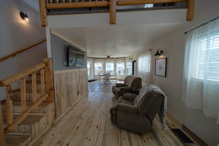 Living room with light wood-type flooring, ceiling fan, and wood walls