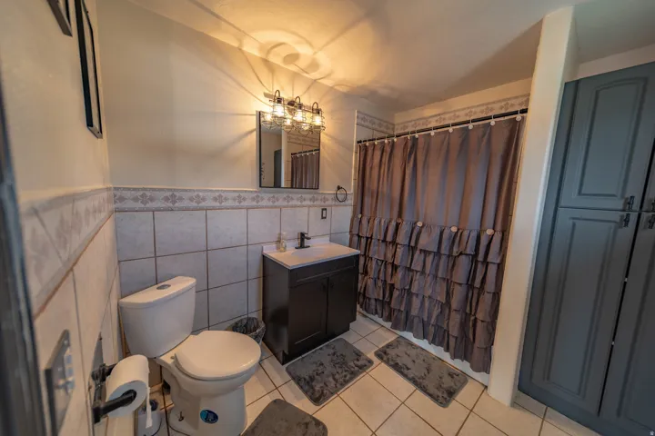 Full bath featuring vanity, curtained shower, tile walls, light tile patterned floors, and wainscoting