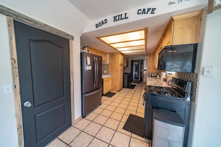 Kitchen featuring black appliances, light countertops, light tile patterned flooring, and light wood finish cabinets