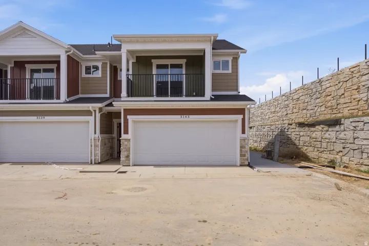 View of front facade with stone siding, an attached garage, and a balcony
