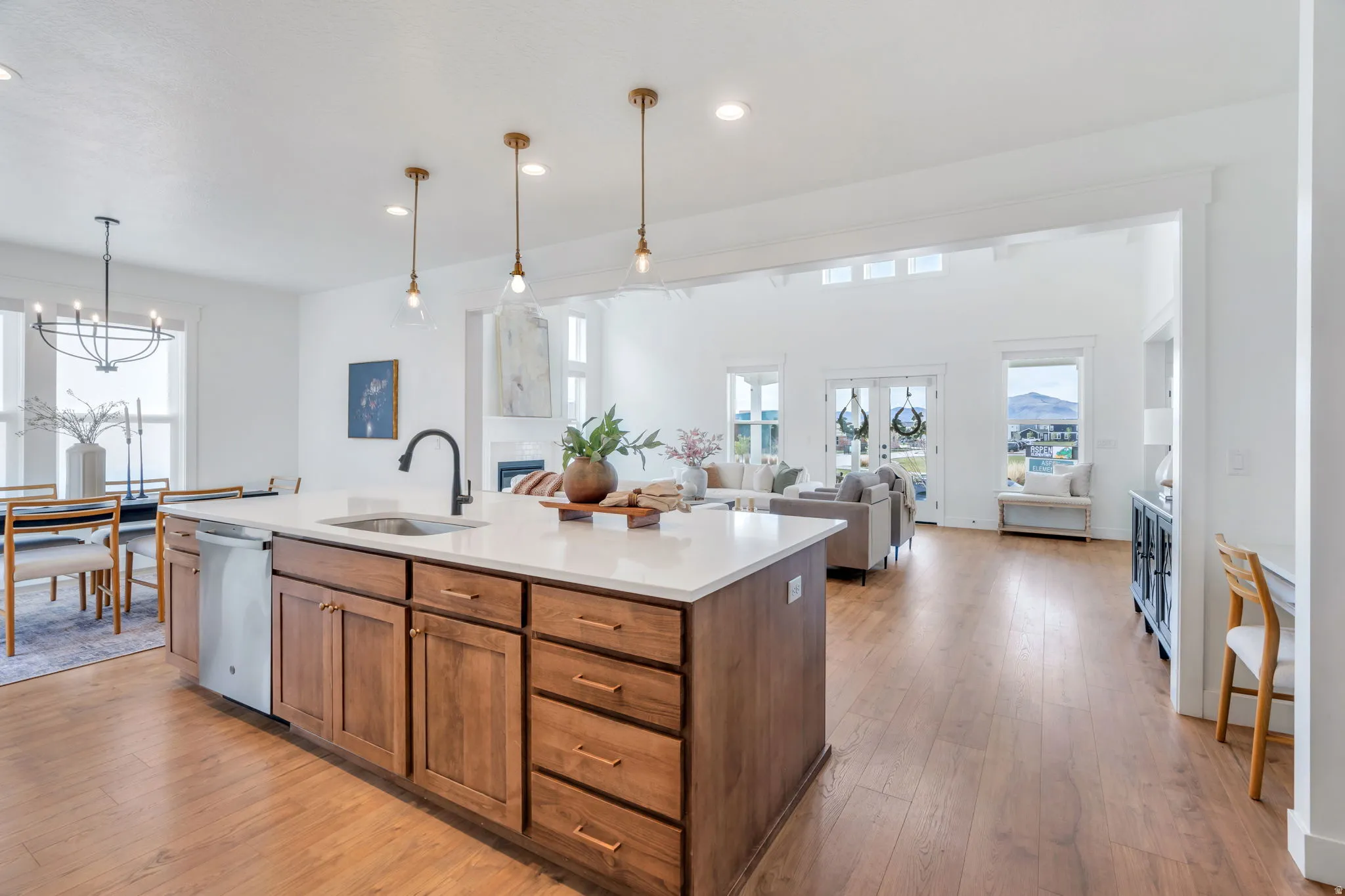 Kitchen with open floor plan, light wood finished floors, an island with sink, stainless steel dishwasher, and wood finish cabinetry