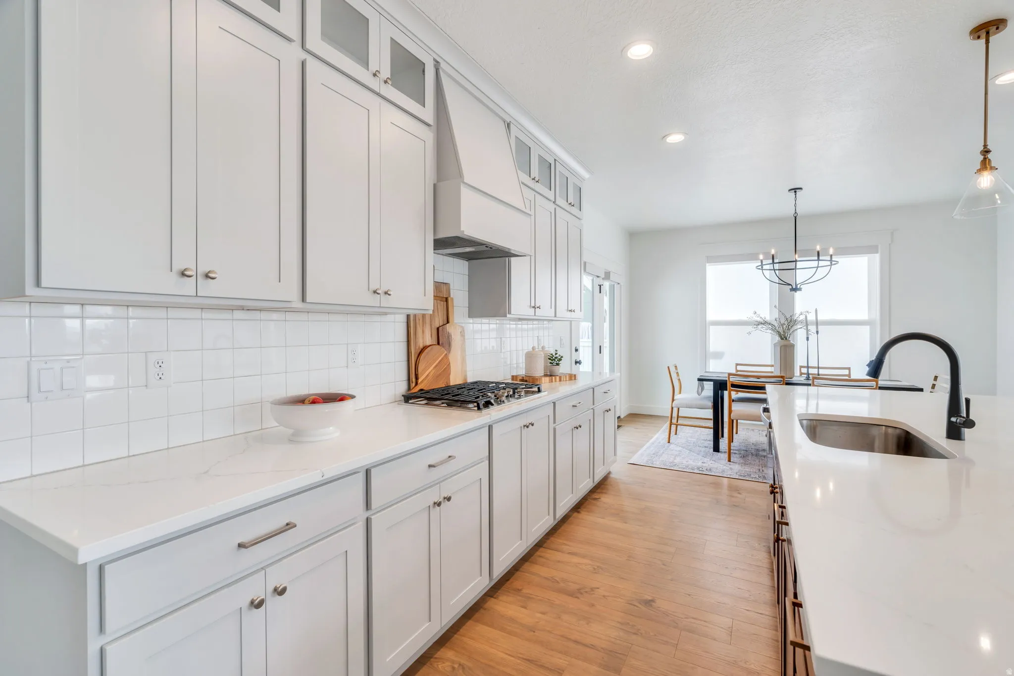 Two tone kitchen featuring glass fronted cabinets, light wood finished floors, light stone counters, tasteful backsplash, and two tone cabinets
