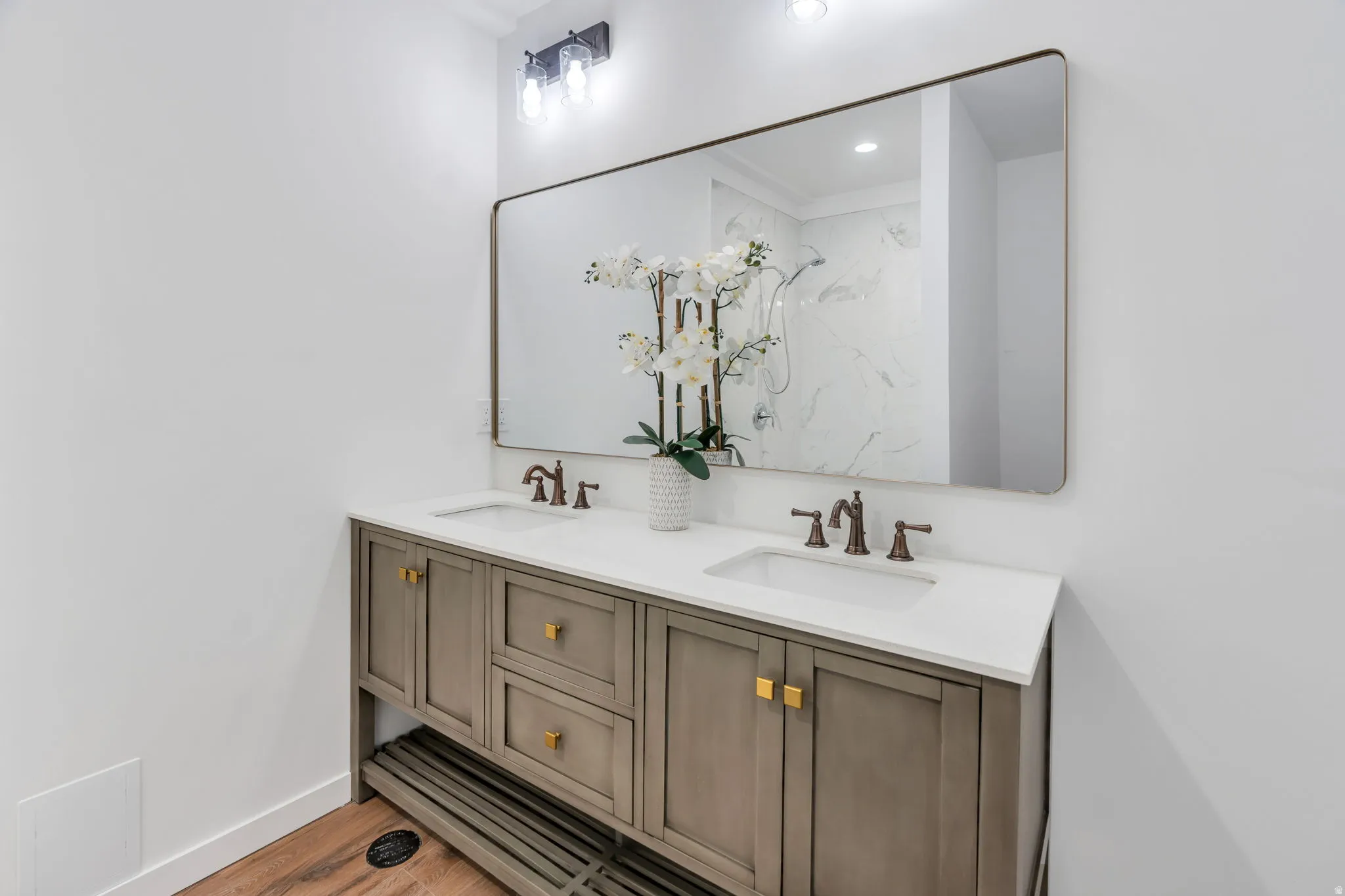 Bathroom featuring double vanity, a marble finish shower, and light wood-type flooring