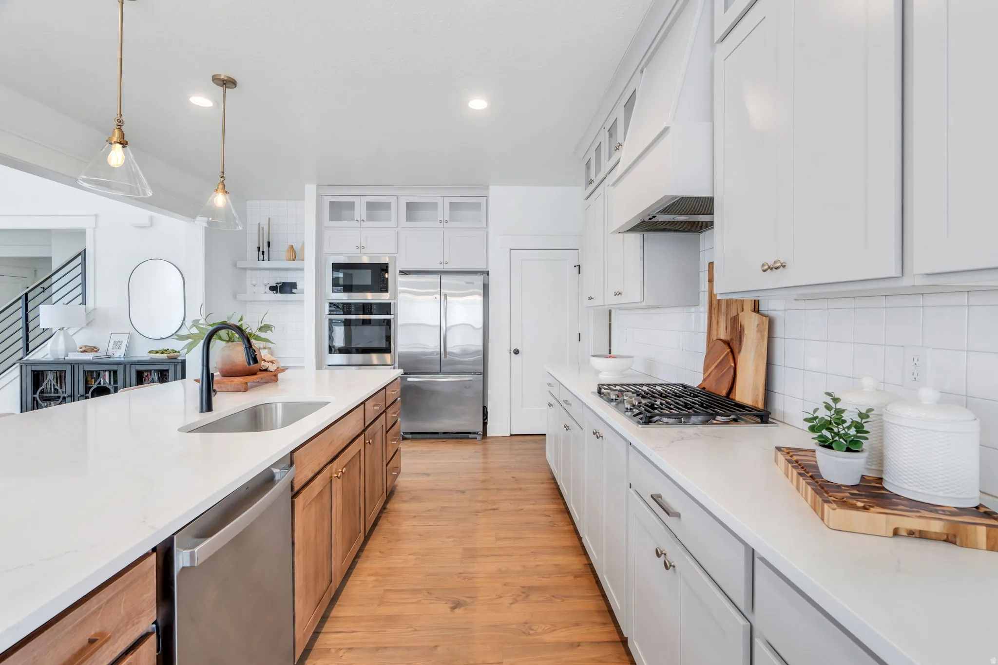 Two tone kitchen featuring dual tone cabinets, hanging light fixtures, stainless steel appliances, glass insert cabinets, and light stone countertops