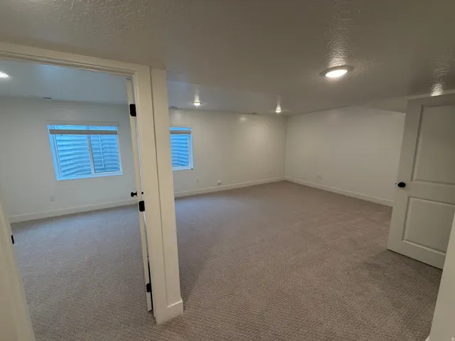 Spacious room featuring neutral carpeting, white walls, recessed lighting, and two windows with blinds