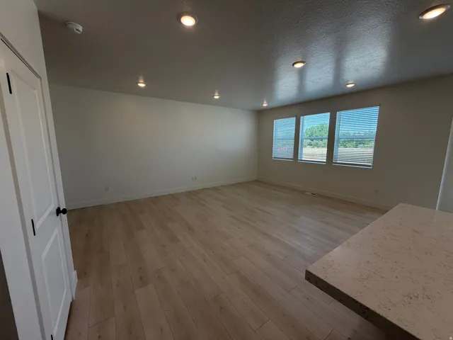 Spacious room featuring wood-finish flooring, white walls, and multiple recessed ceiling lights