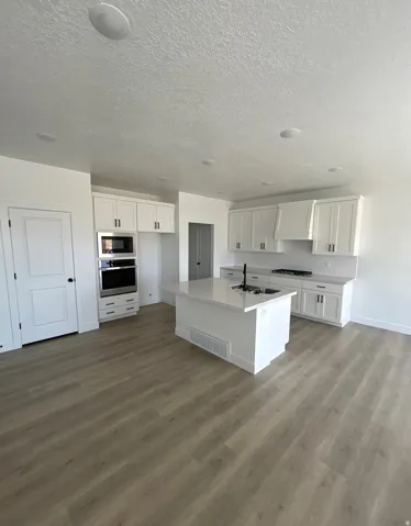 Kitchen with white cabinetry, stainless steel appliances, a center island with sink, light wood-style flooring, and a textured ceiling